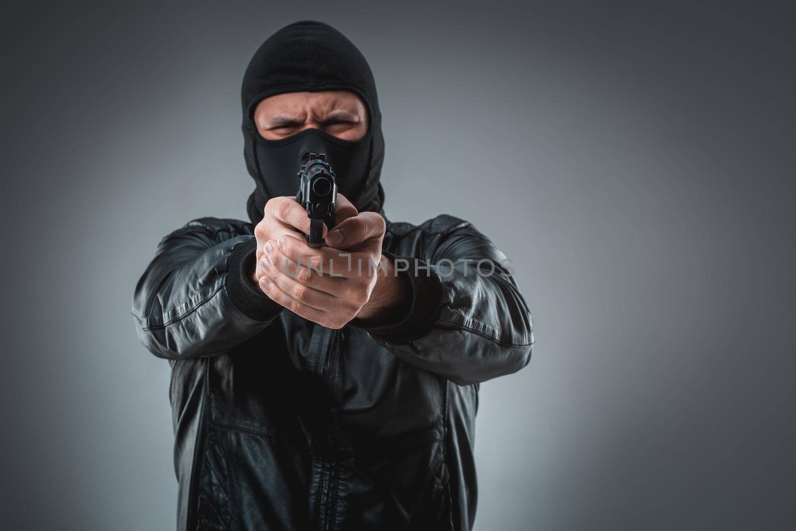 Burglar or terrorist in black mask shooting with gun. A man in the studio on a black-and-gray background