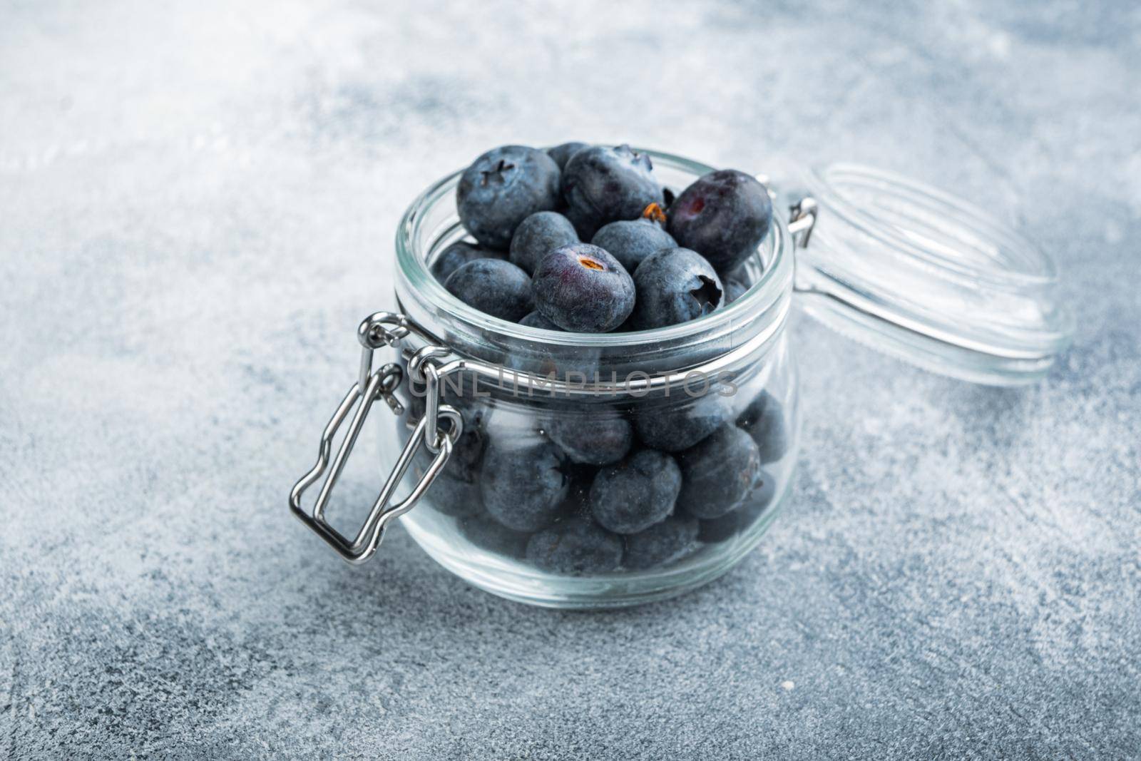 Ripe blueberry in glass jar, on textured background.