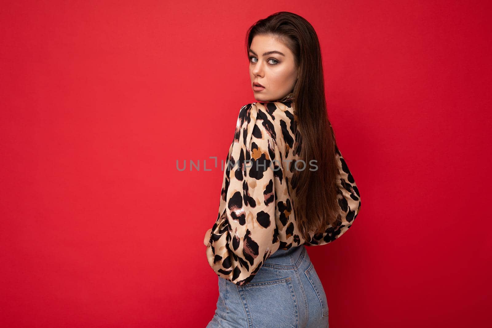 Image of a beautiful young brunette woman dressed in animal printed blouse posing isolated over red background with copy space.