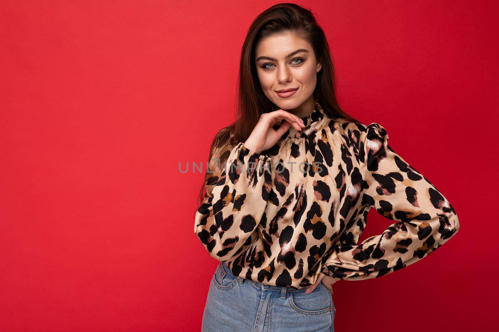 Image of a beautiful young brunette woman dressed in animal printed blouse posing isolated over red background with copy space.