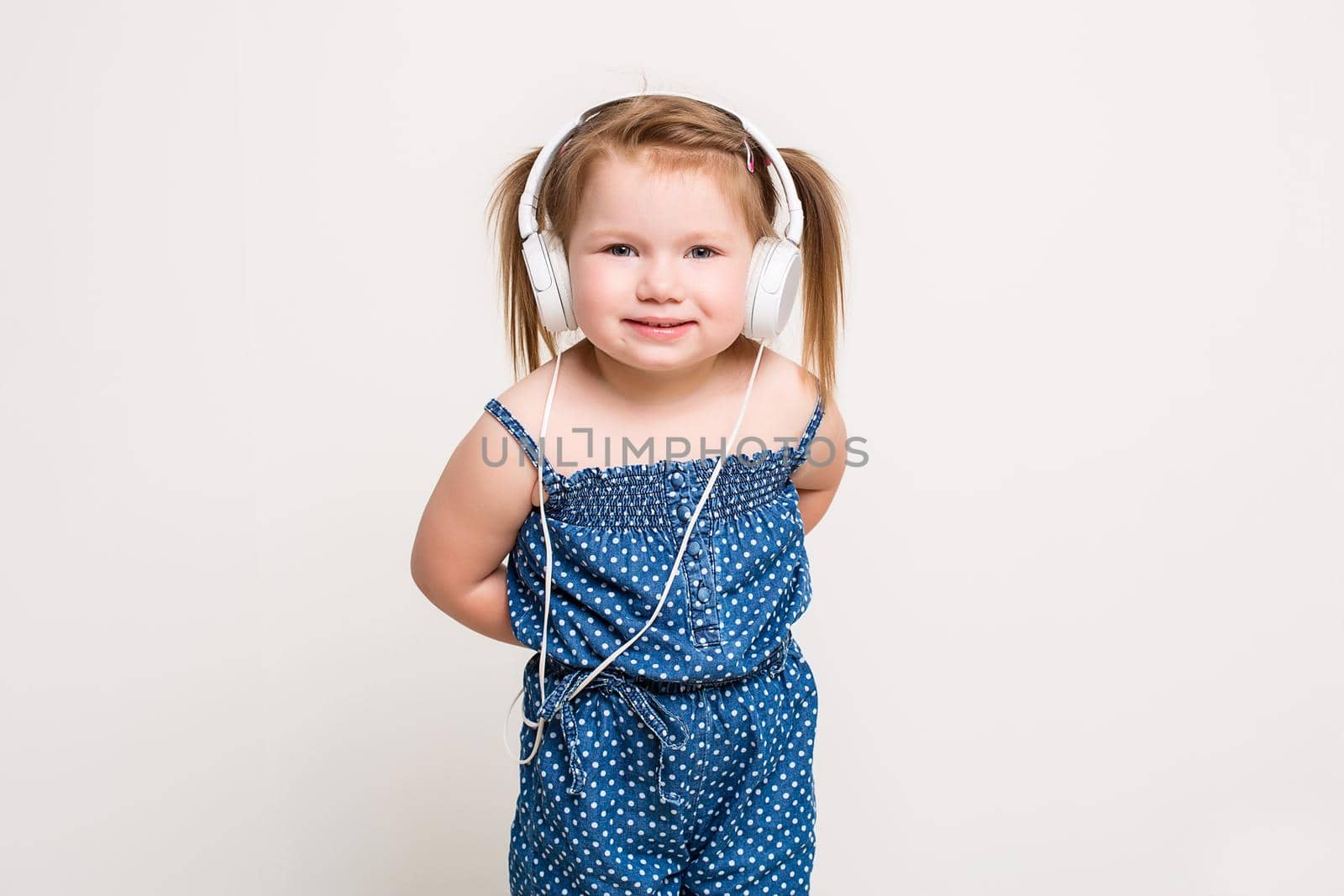 Cute little girl in headphones listening to music using a tablet and smiling on white background. A child looks at the camera