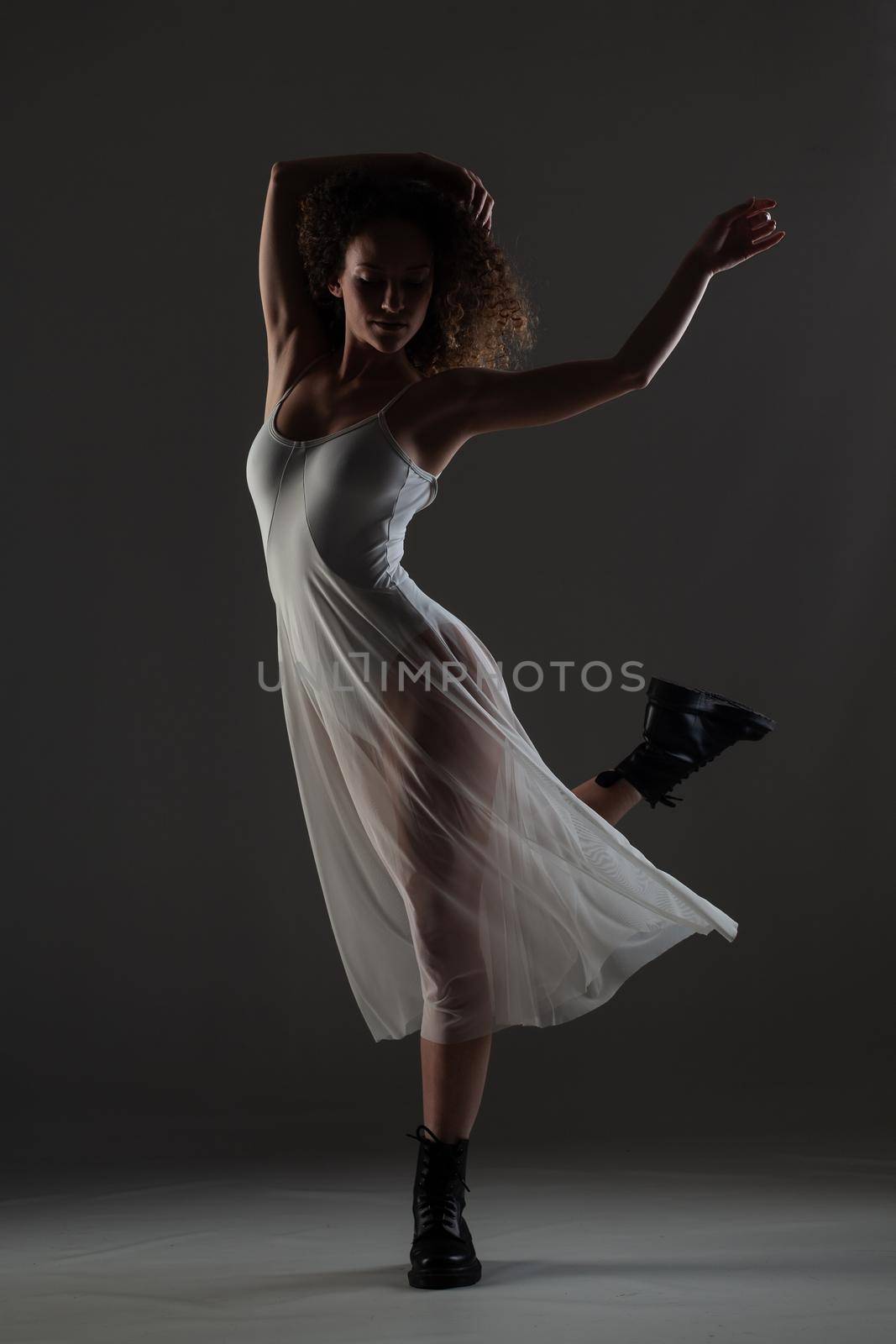 Girl with curly hair making ballet poses. Ballerina in white dress and black boots.