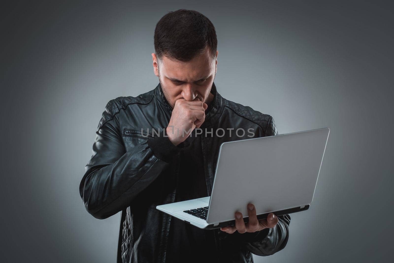 Man in black jacket looking at laptop, half turn. Holding opened laptop and working. Emotion. Indoors, studio, waist up, profile