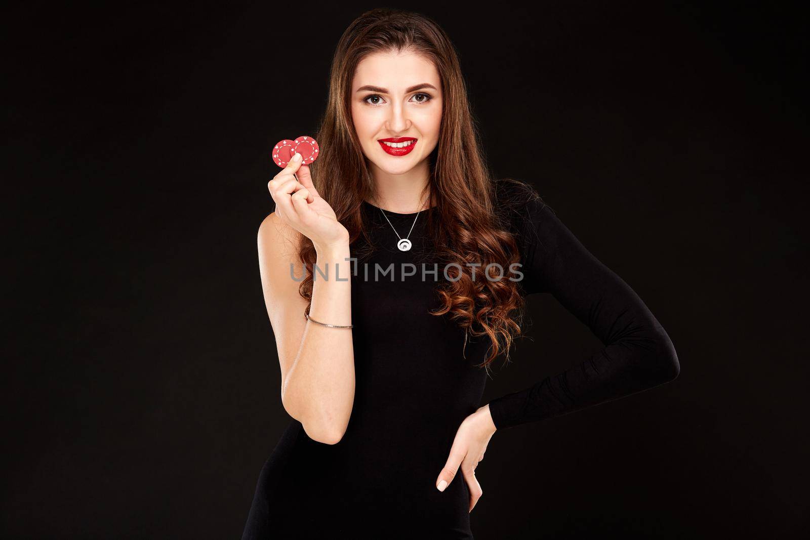 Sexy curly hair brunette in black dress posing with chips in her hands, poker concept black background. Casino, poker, Roulette Blackjack Spin.