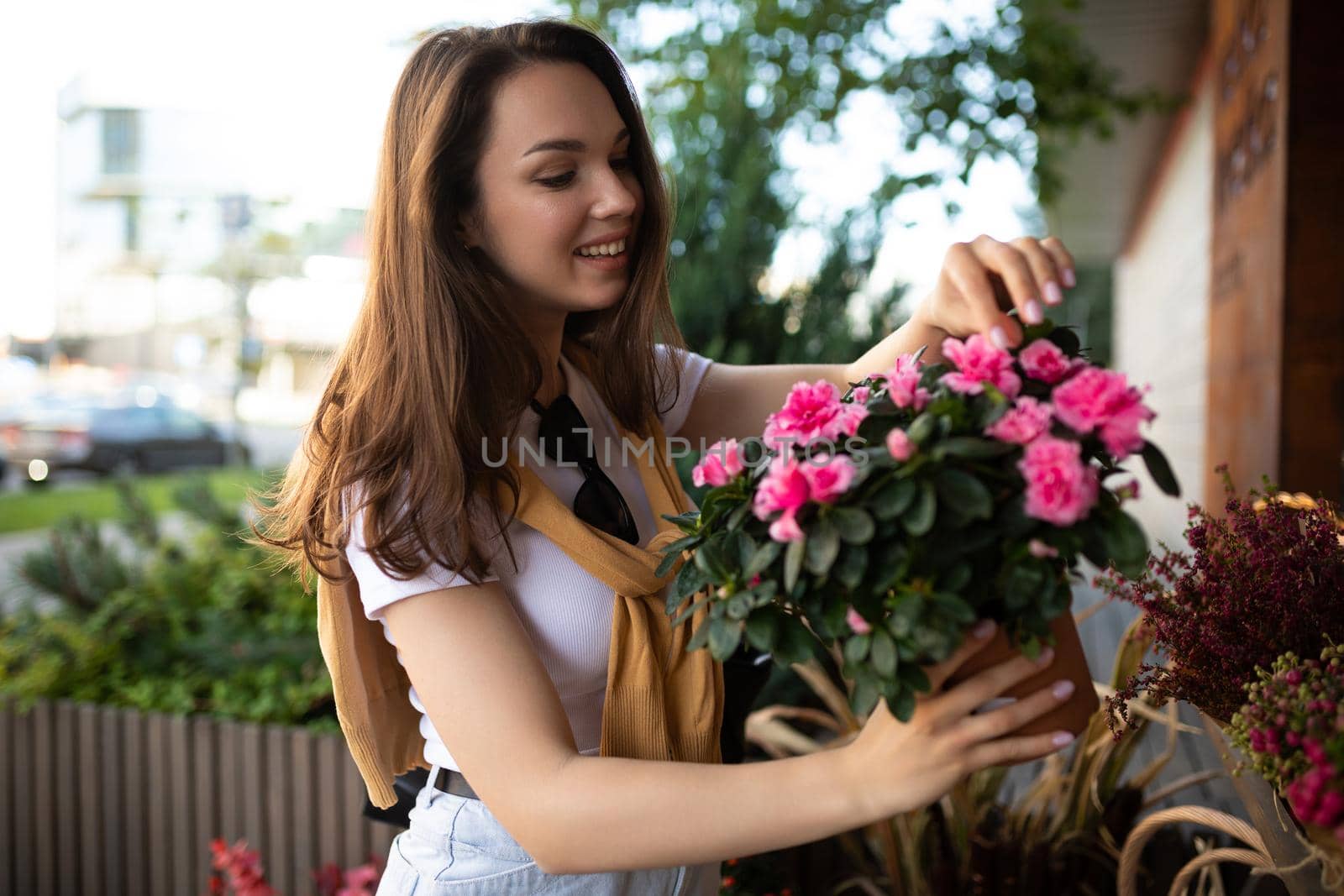 young beautiful brunette woman enjoying flowers in pots on the porch of a flower shop.