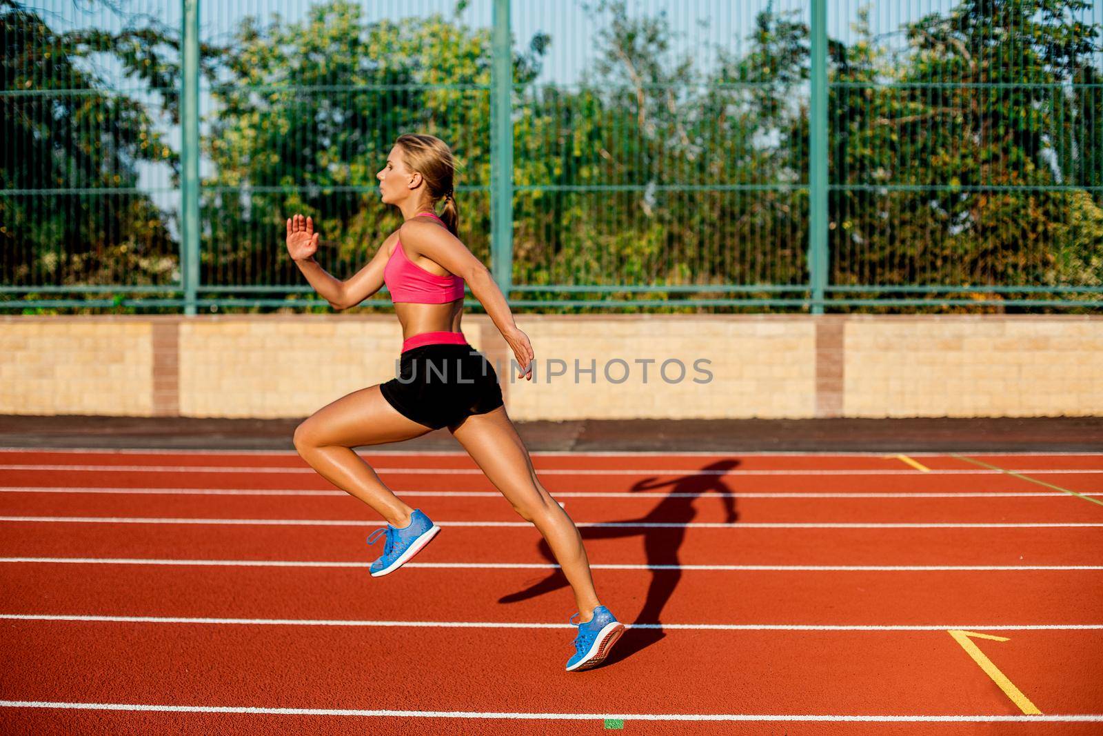 Side view beautiful young woman exercise jogging and running on athletic track on stadium. Sport, healthy lifestyle concept.