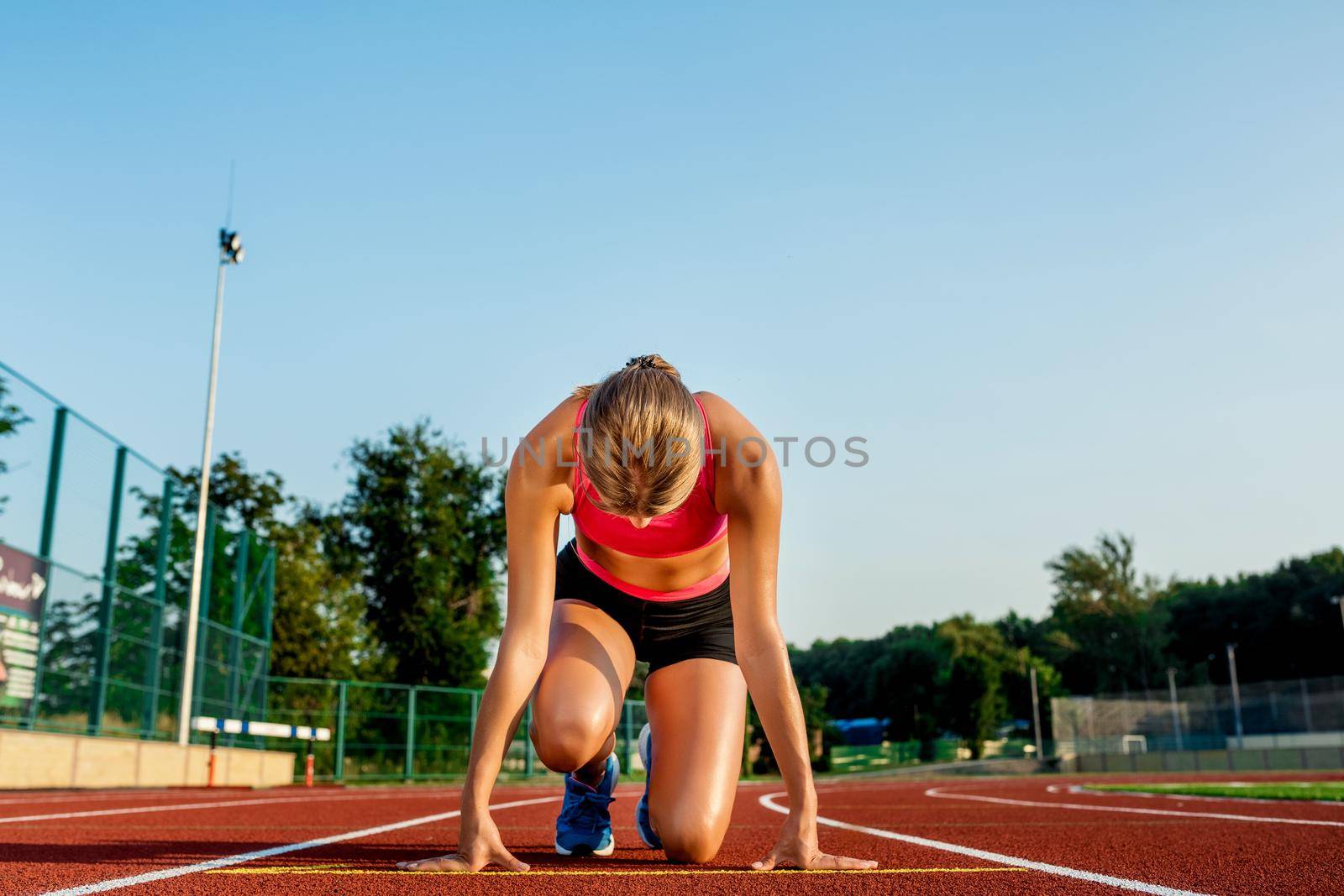 Young woman athlete at starting position ready to start a race. Female sprinter ready for sports exercise on racetrack.