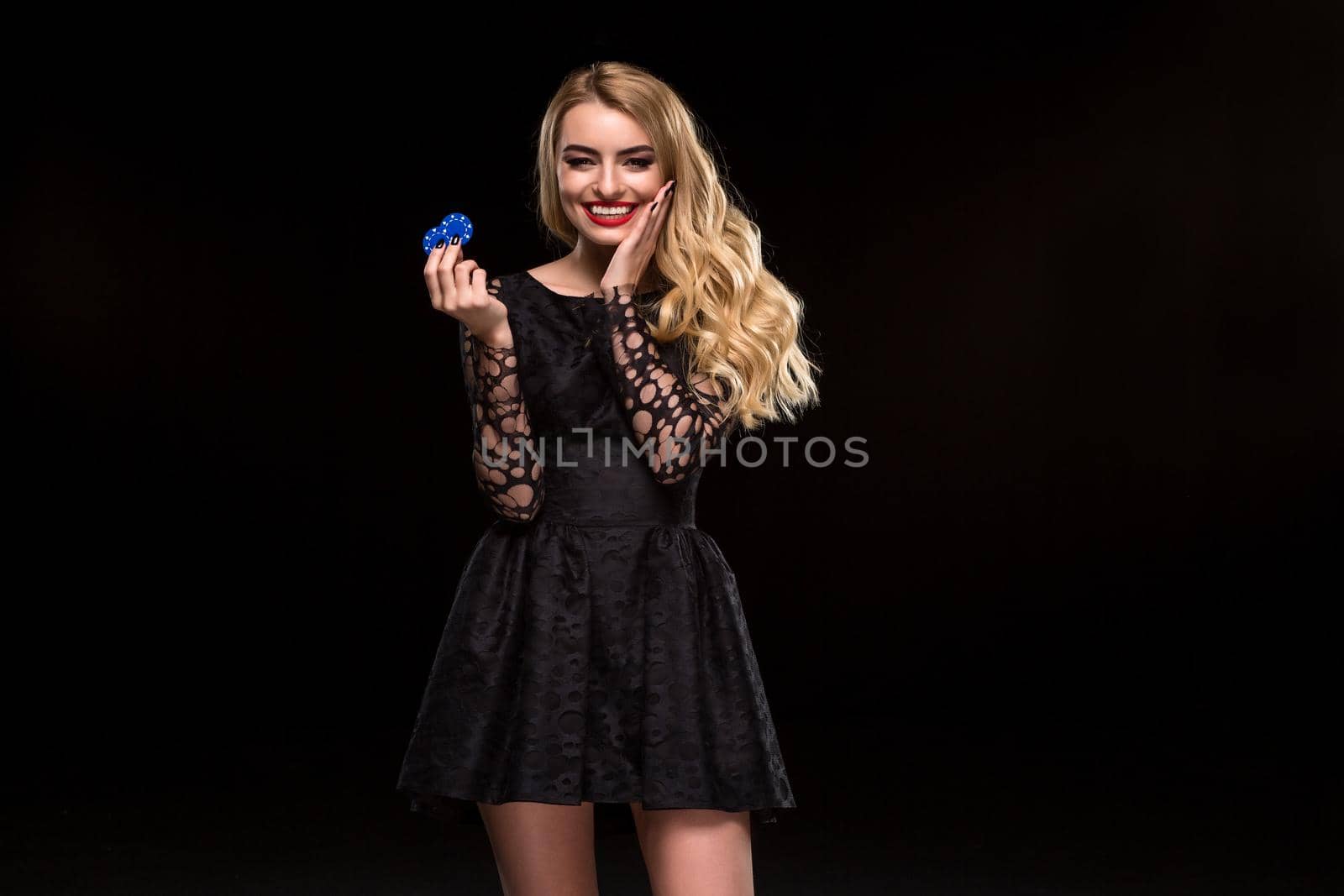 Beautiful blonde in a black dress with casino chips in hands isolated on a black background. Poker. Casino. Roulette Blackjack Spin. Caucasian young woman looking at the camera