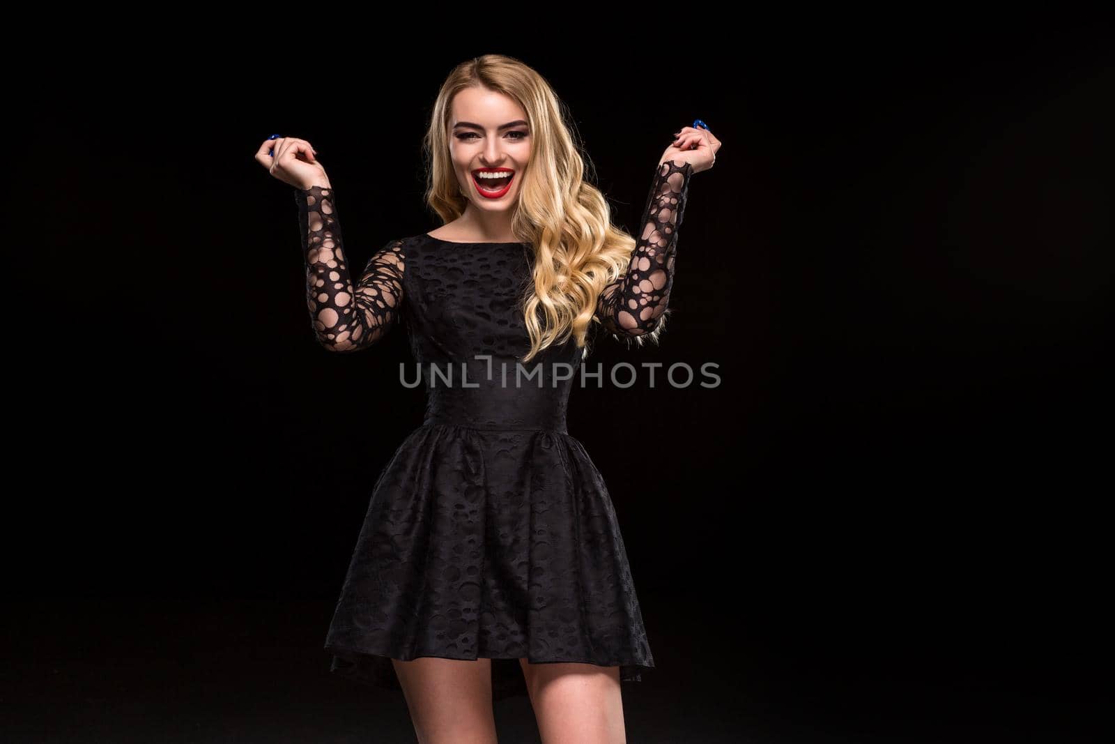 Beautiful blonde in a black dress with casino chips in hands isolated on a black background. Poker. Casino. Roulette Blackjack Spin. Caucasian young woman looking at the camera