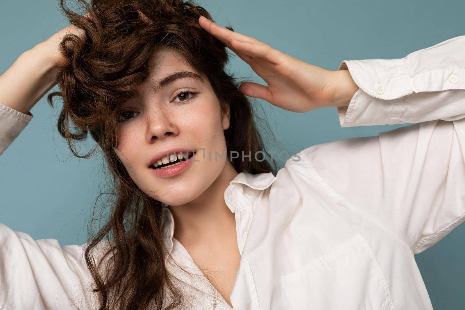 Attractive cute nice adorable tender young curly brunette woman wearing white shirt isolated on blue background.