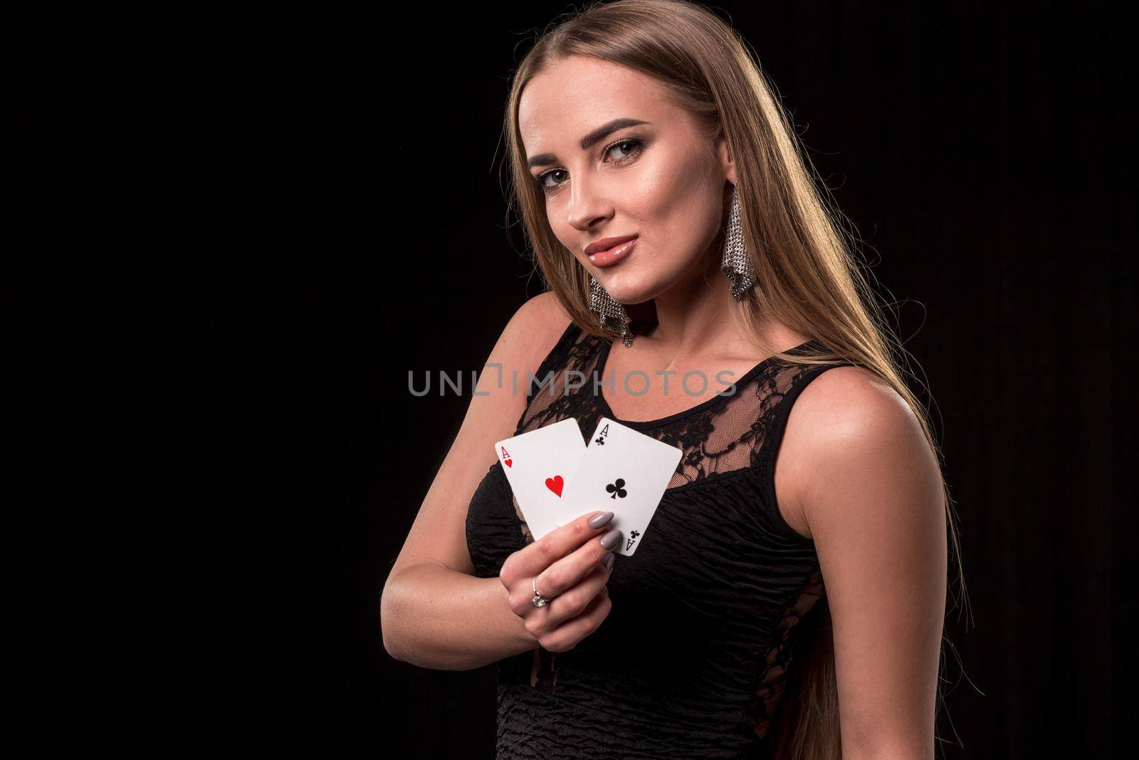 Young beautiful woman in a sexy black dress playing in casino. Girl holding the winning combination of poker cards on a black background. Two aces