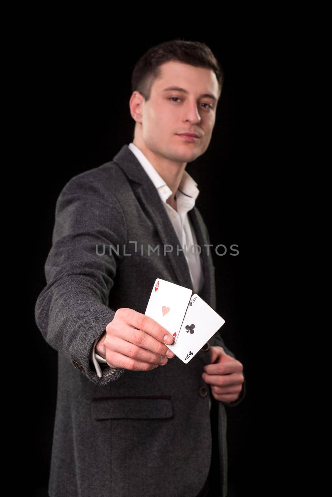 Young caucasian man wearing suit holding two aces in his hand on black background. Gambling concept. Casino by nazarovsergey