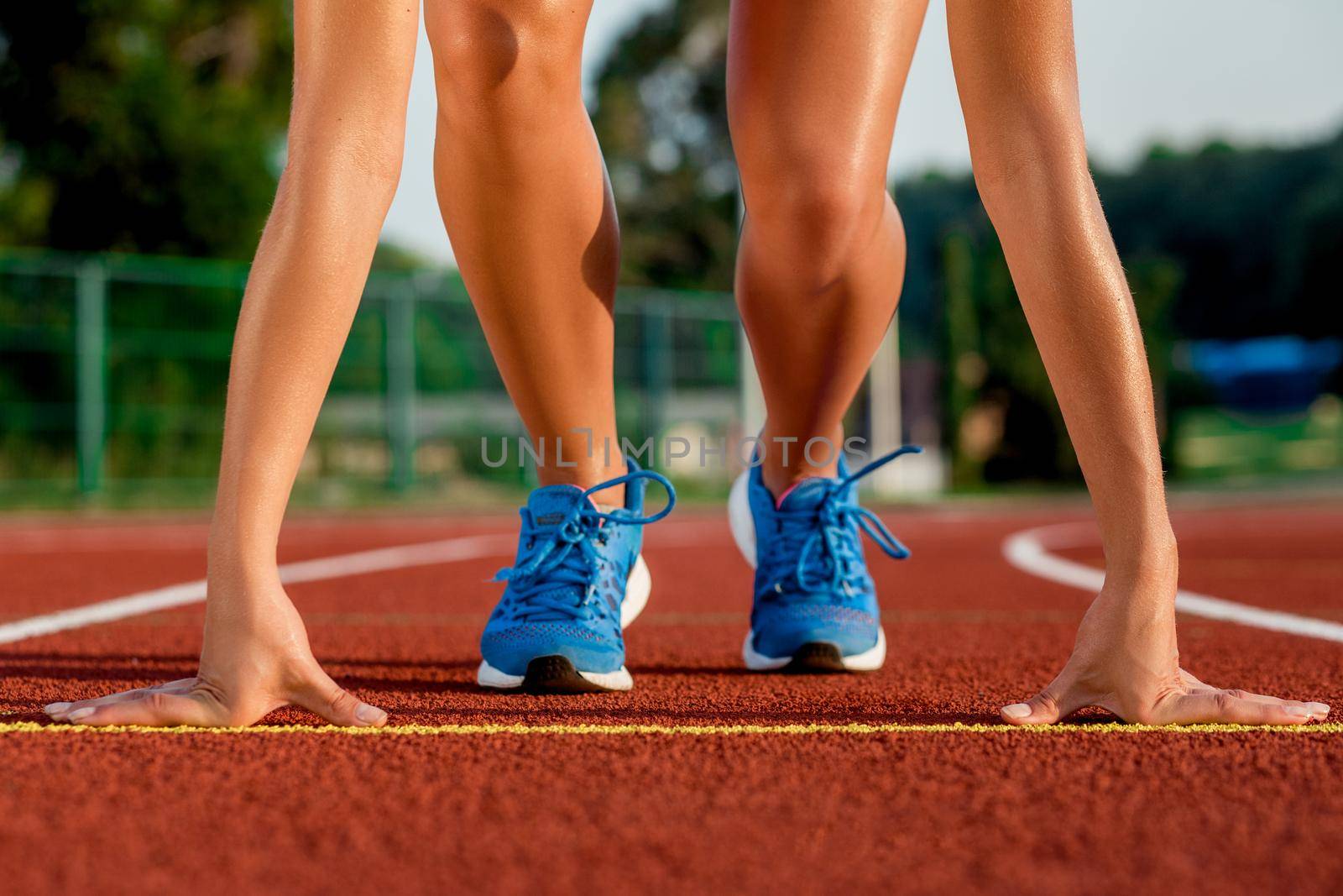 Close-up of woman's legs in blue sneakers on start before jogging. Red treadmill at the stadium