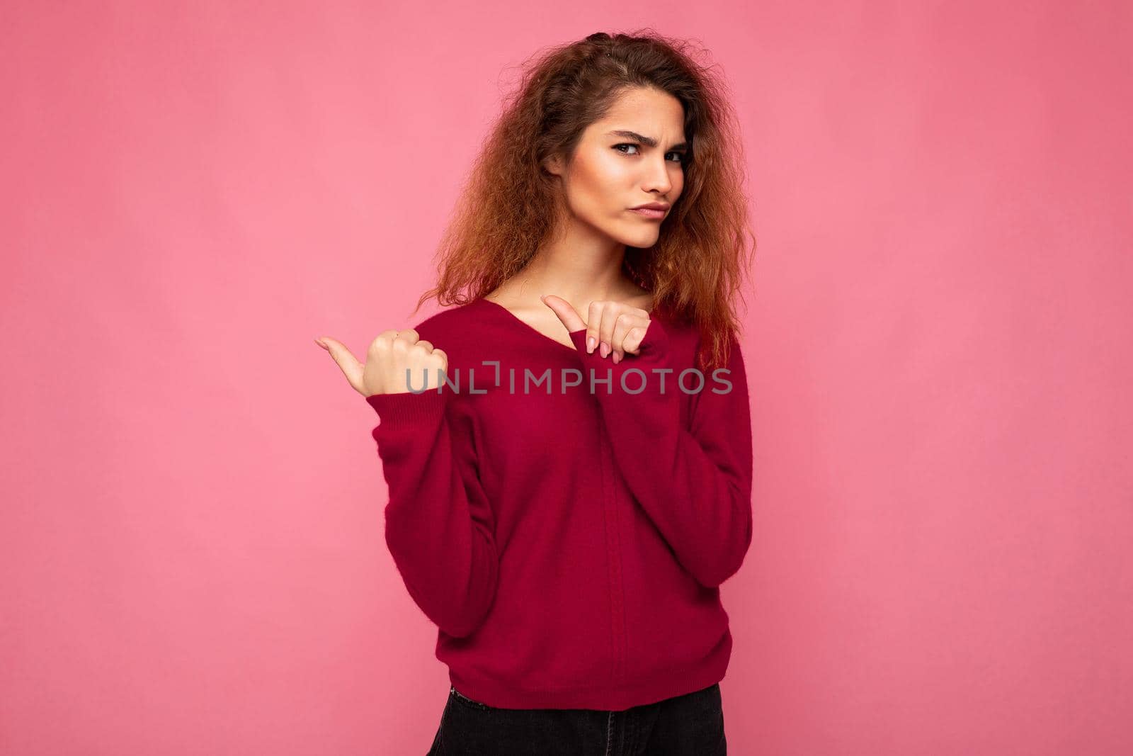 Photo of young beautiful brunette wavy woman with sincere emotions wearing casual pink jersey isolated over pink background with copy space and pointing at free space for mockup.