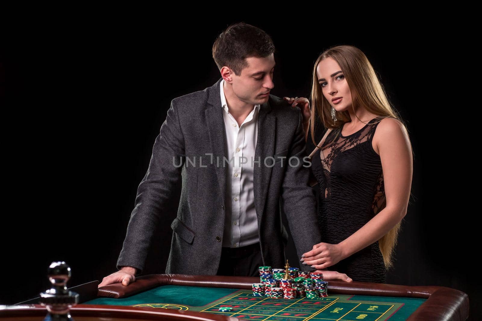 Elegant couple at the casino betting on the roulette, on a black background. A man in a suit with a beautiful young woman in a black dress