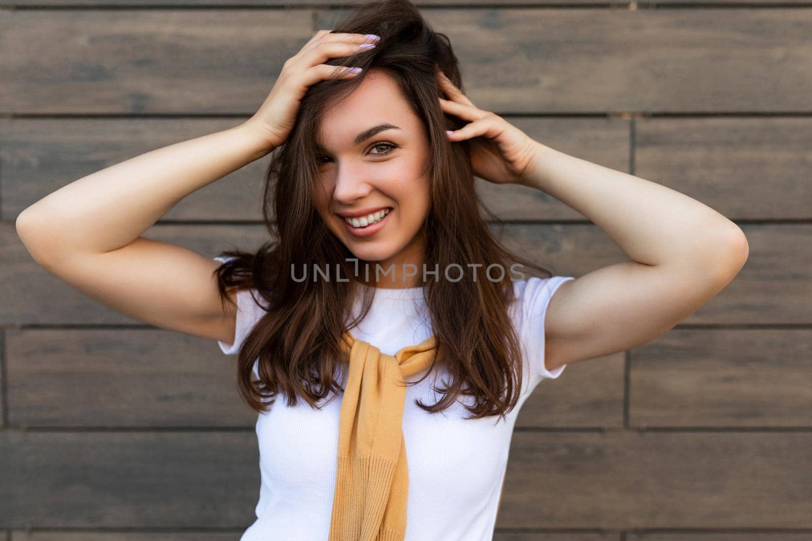 Close-up photo of pretty attractive beautiful smiling happy positive charming young brunette young woman wearing stylish clothes in the street near brown wall.