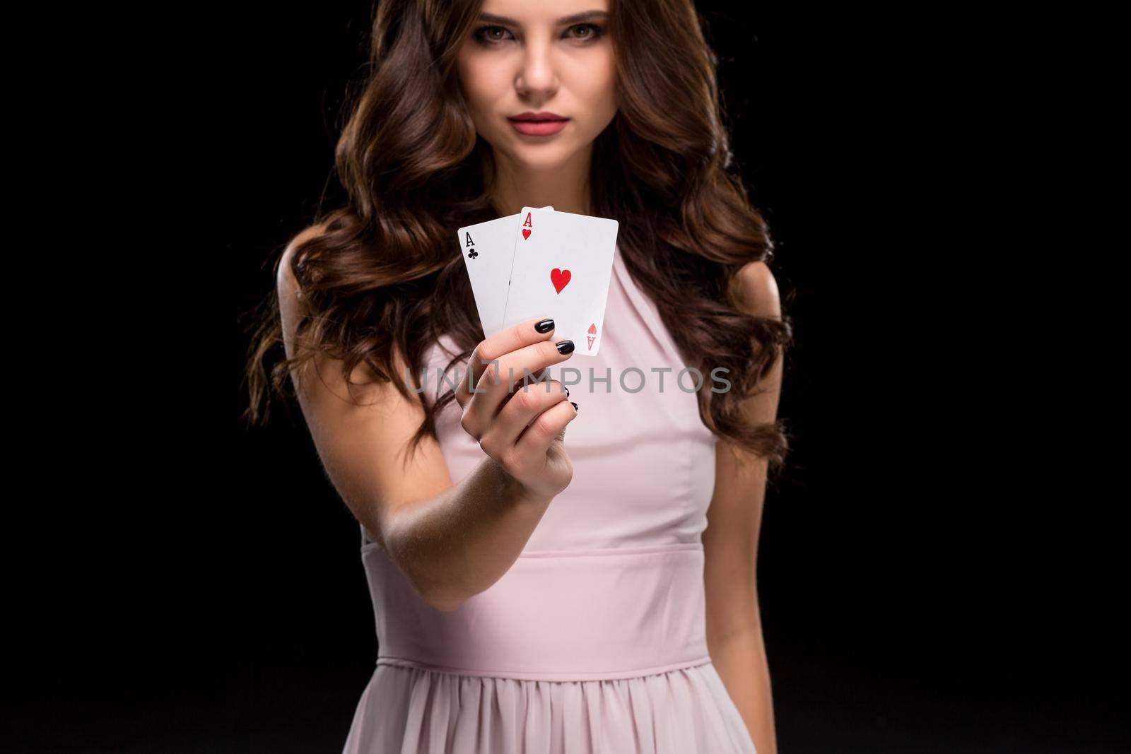 Sexy brunette woman in a chic gently pink dress, holding aces winning hand on a black background. Focus on poker cards in hands. Poker. Victory. Luck