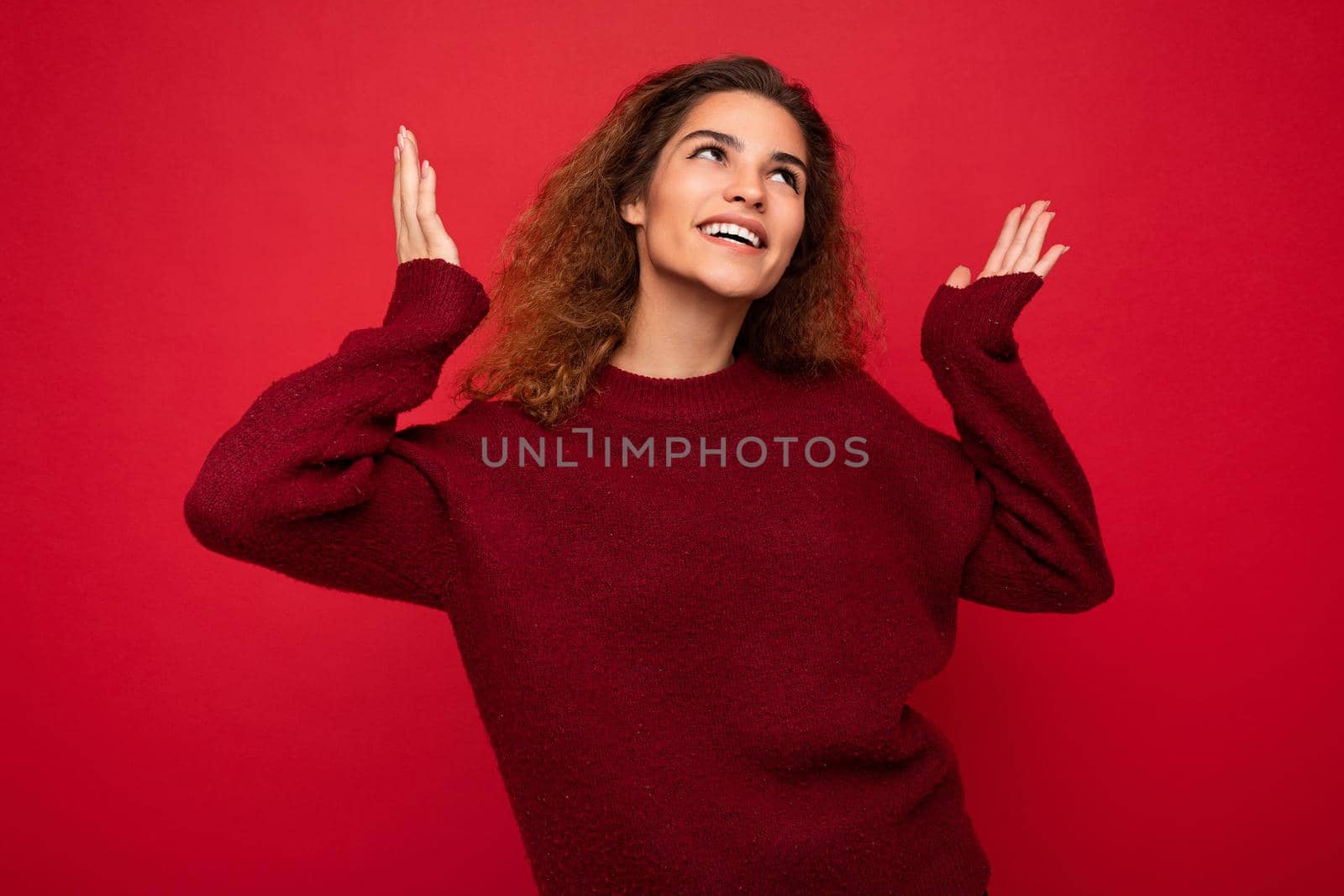 Young beautiful curly brunette woman with sincere emotions poising isolated on background wall with copy space wearing casual dark red sweater. fun and joy concept.