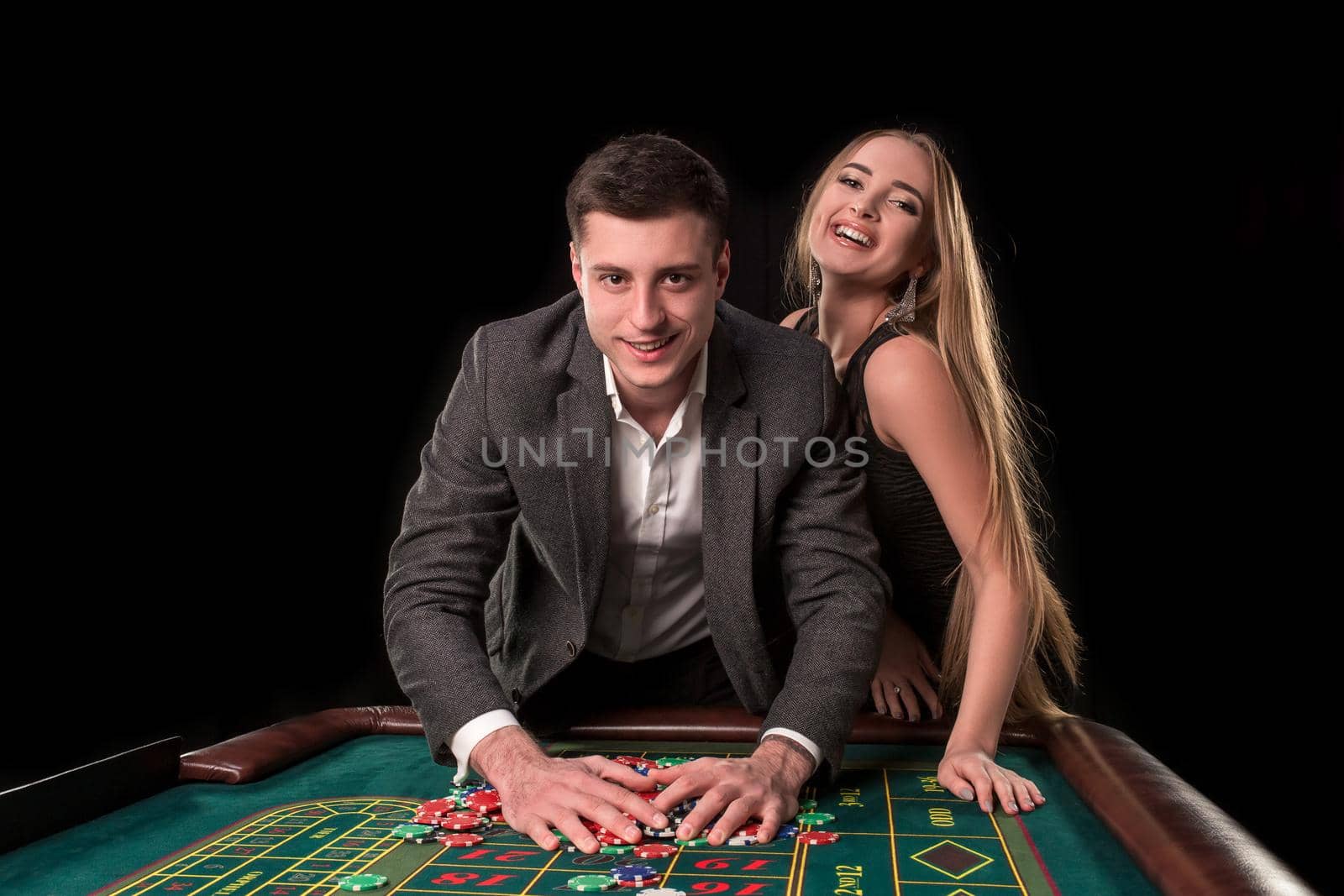 Young beautiful couple takes their winnings at the roulette table at the casino by nazarovsergey