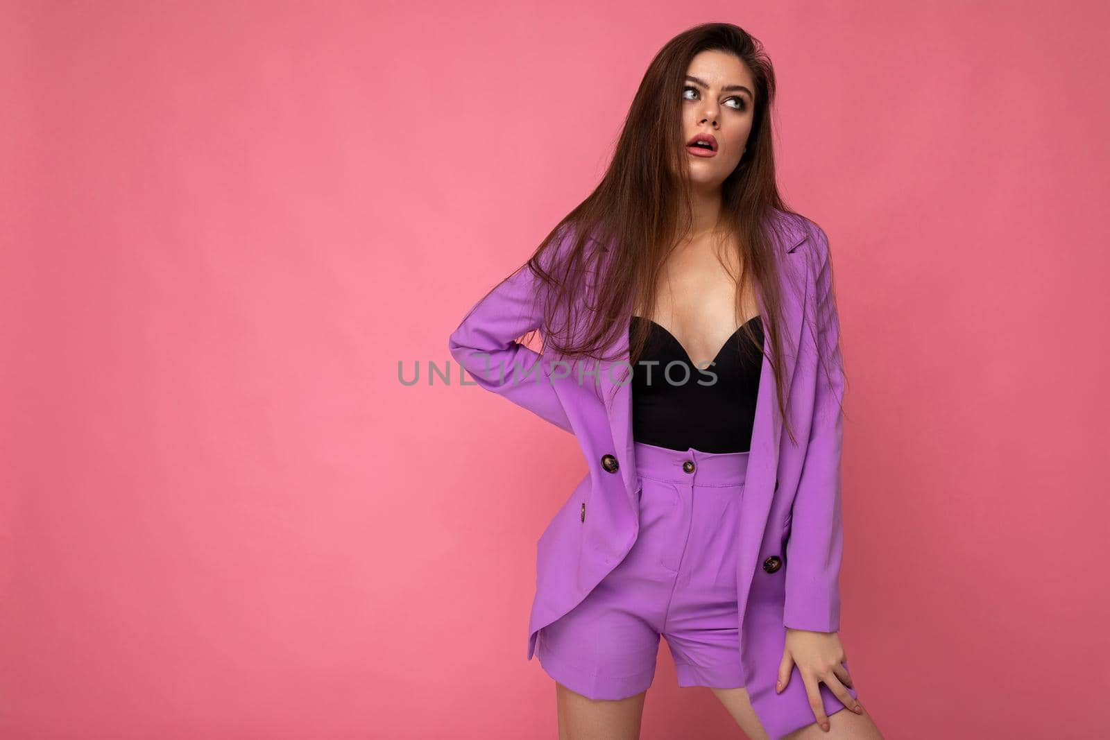 Portrait of young dissatisfied attractive fashionable brunette woman wearing stylish violet suit isolated on pink background with empty space. Business concept.
