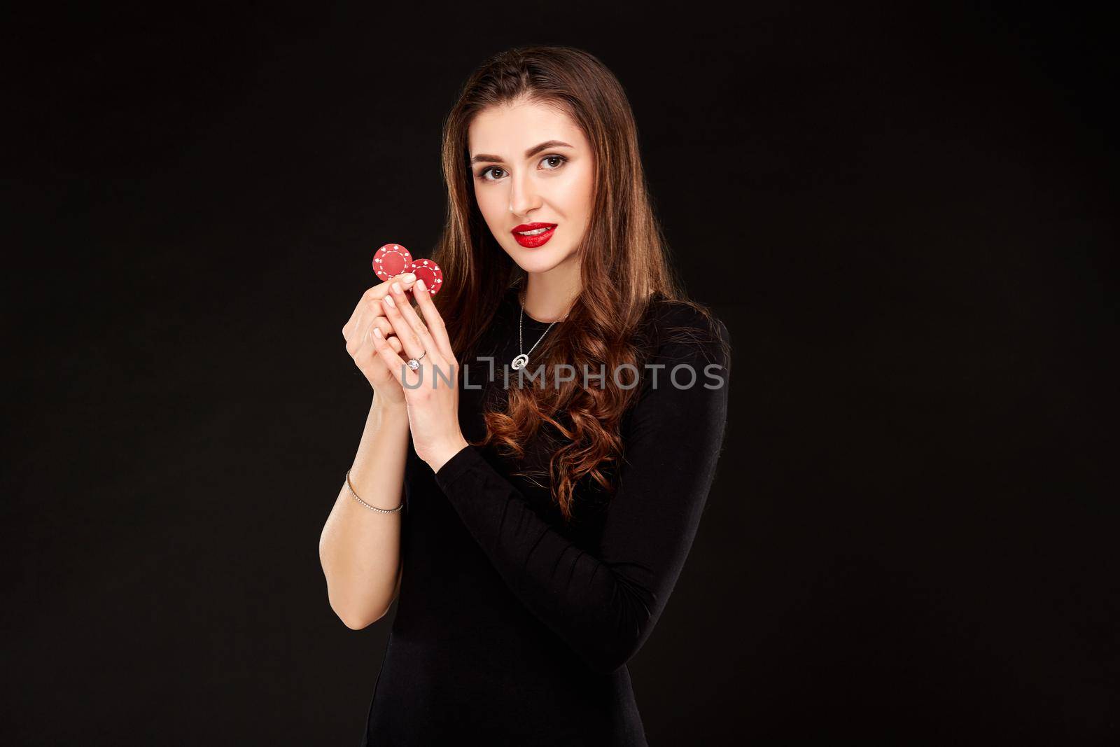 Sexy curly hair brunette in black dress posing with chips in her hands, poker concept black background. Casino, poker, Roulette Blackjack Spin.