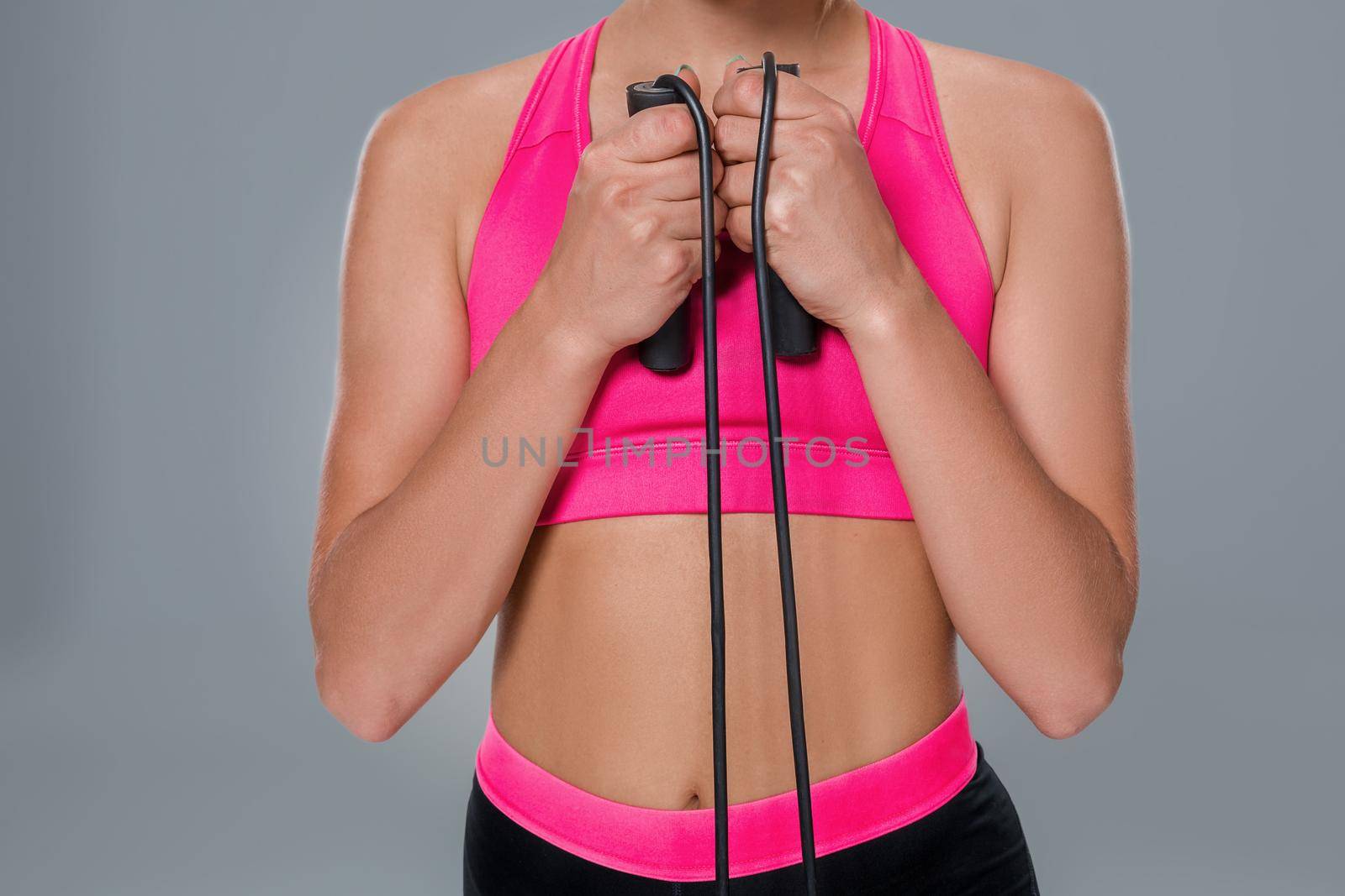 Full length image of a pretty fitness woman doing exercise with skipping rope over gray background. Close-up by nazarovsergey