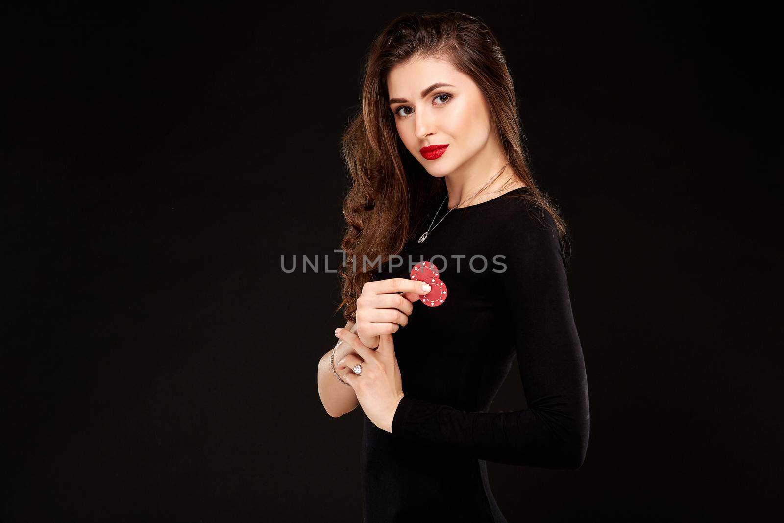 Sexy curly hair brunette in black dress posing with chips in her hands, poker concept black background. Casino, poker, Roulette Blackjack Spin.