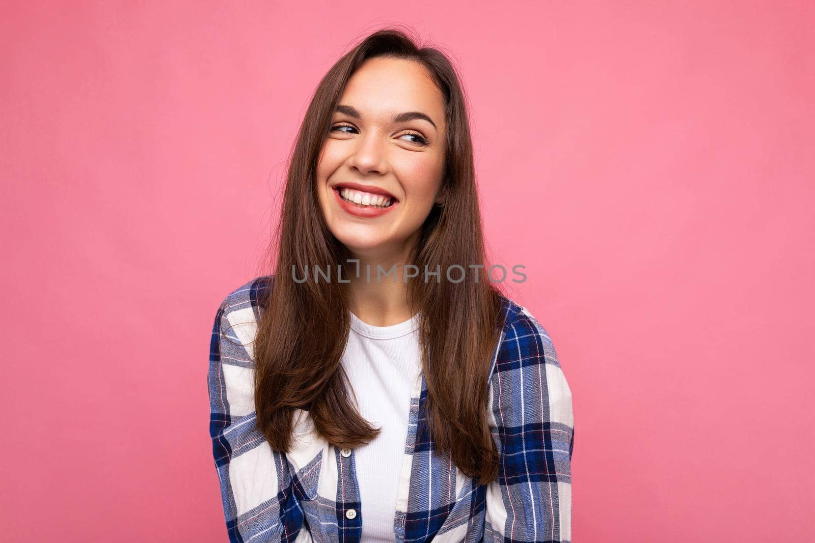 Photo portrait of young beautiful smiling hipster brunette woman in trendy blue and white shirt. Sexy carefree female person posing isolated near pink wall with empty space in studio. Positive model.