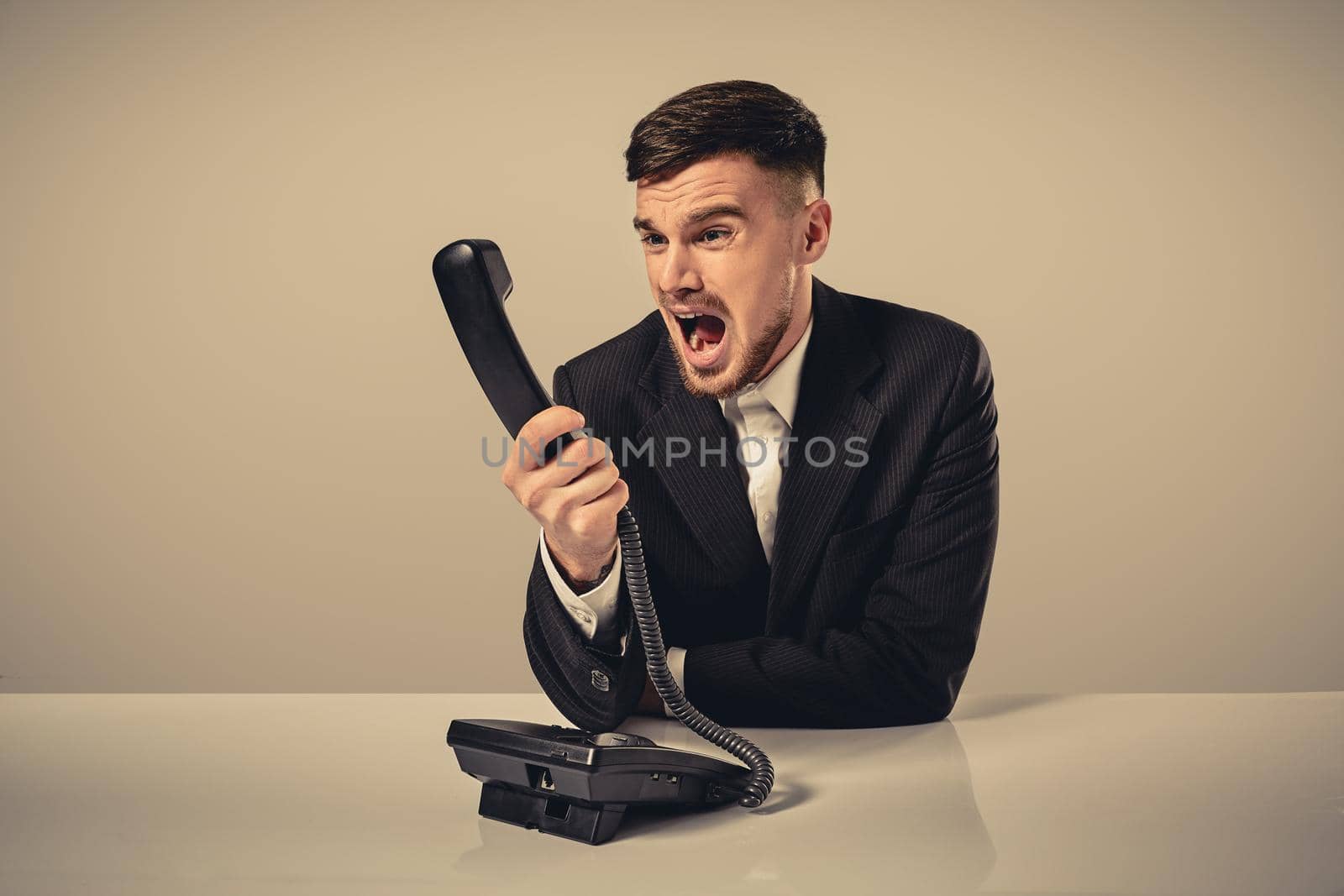 A young man in a black suit dials the phone number while sitting in the office. Manager talking on the phone. Man emotionally shouts