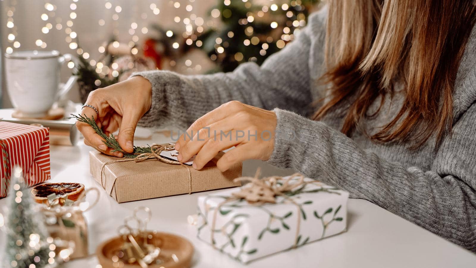 Woman s hands wrapping Christmas gift boxes, close up. Unprepared presents on white table with decor elements and items Christmas or New year DIY packing Concept.