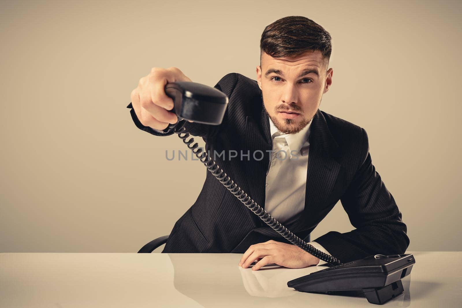 Portrait of attractive businessman holding telephone in his hand. This call is for you concept. A young man in a black suit dials the phone number while sitting in the office