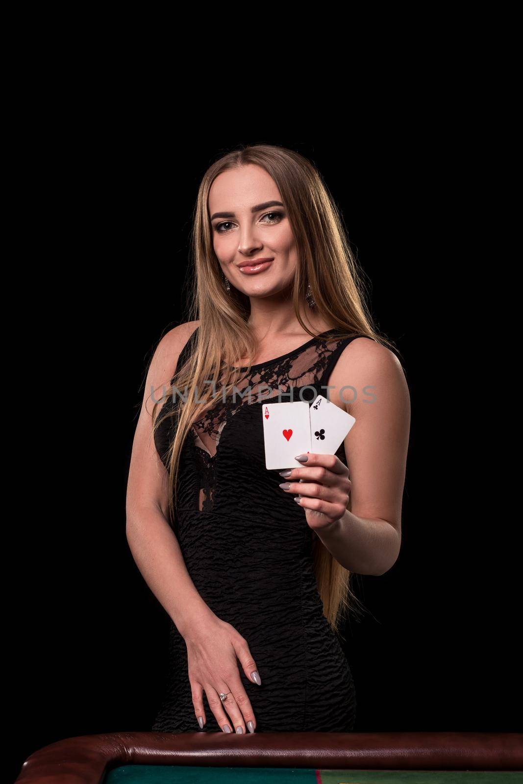 Young beautiful woman in a sexy black dress playing in casino. Girl holding the winning combination of poker cards on a black background. Two aces