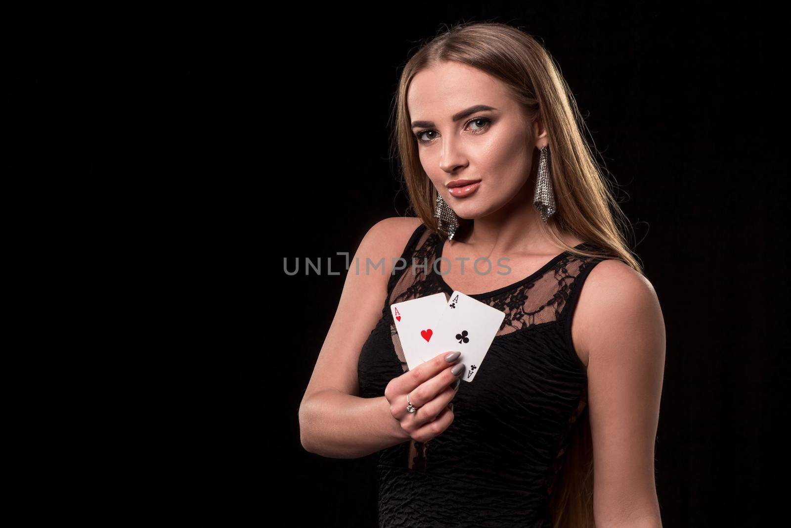 Young beautiful woman in a sexy black dress playing in casino. Girl holding the winning combination of poker cards on a black background. Two aces