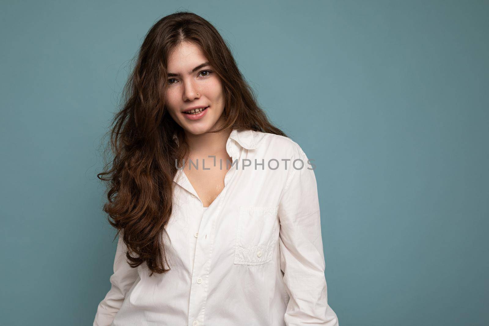 Attractive cute nice adorable tender young curly brunette woman wearing white shirt isolated on blue background with copy space by TRMK