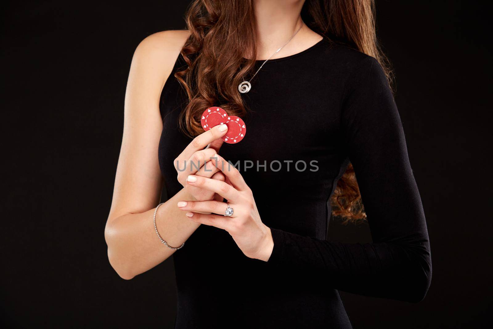 Sexy curly hair brunette in black dress posing with chips in her hands, poker concept black background. Casino, poker, Roulette Blackjack Spin.