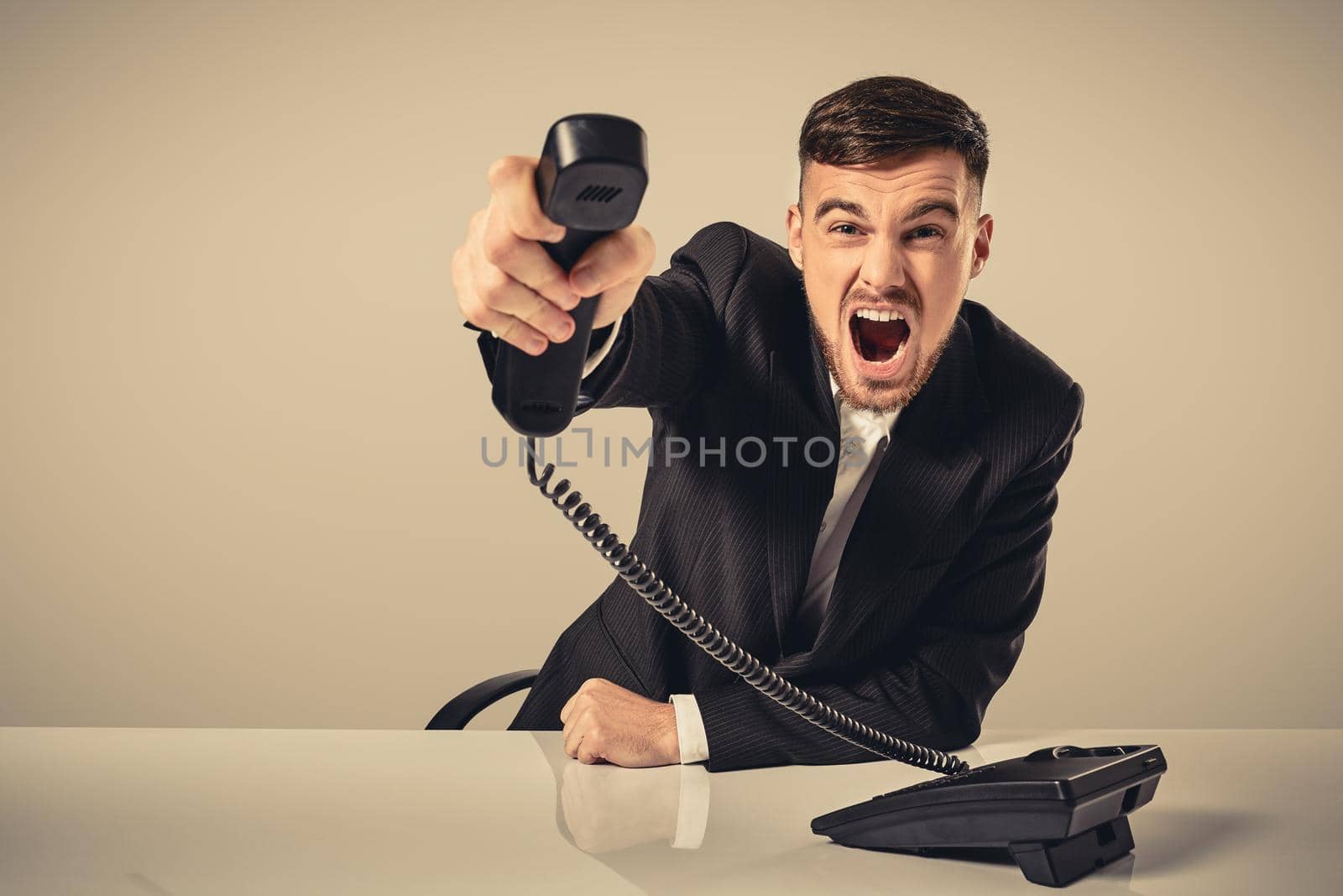 A young man in a black suit dials the phone number while sitting in the office. Manager talking on the phone. Man emotionally shouts