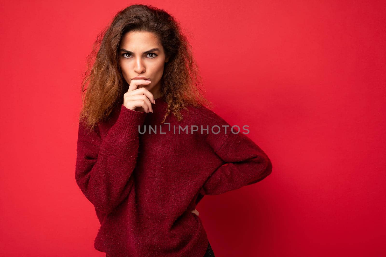 Young beautiful thoughtful serious curly brunette woman with sincere emotions poising isolated on background wall with copy space wearing casual dark red sweater. Think concept.