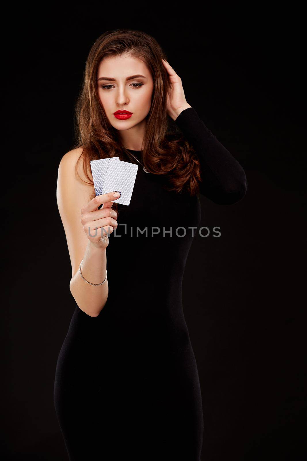 Beautiful confident woman in a sexy black dress showing and looking at poker cards with copy place. Studio shot on a black background. Casino