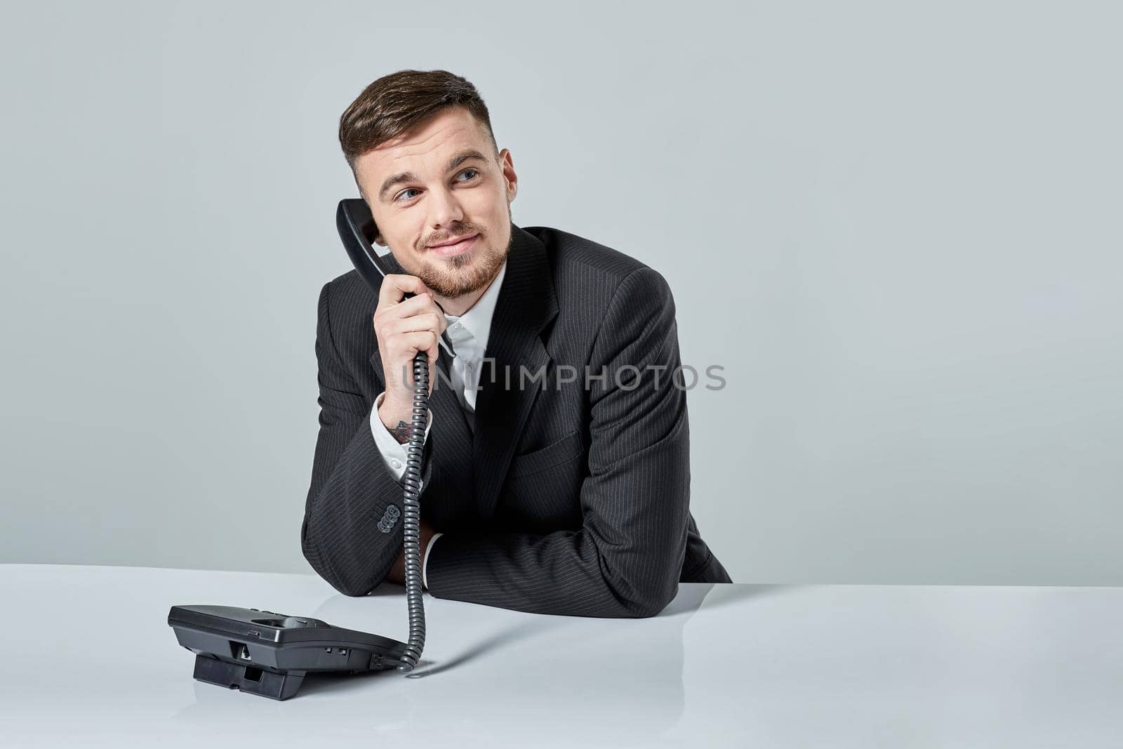 A young man in a black suit dials the phone number while sitting in the office. Manager talking on the phone