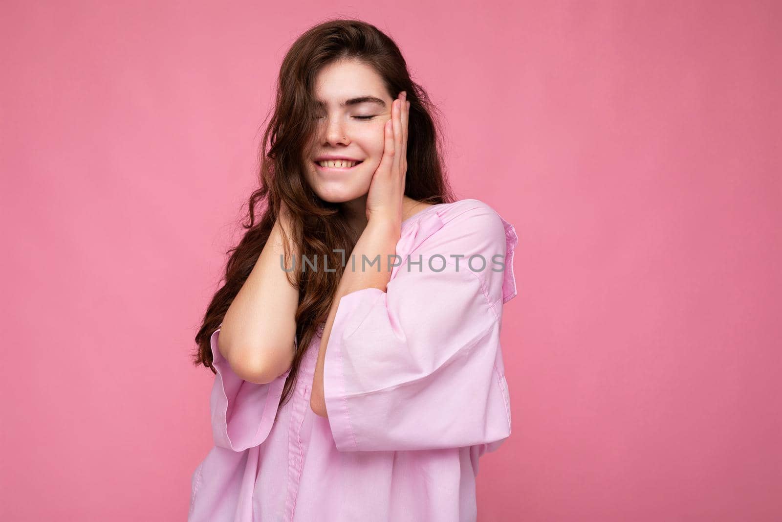 Photo of young positive happy smiling beautiful woman with sincere emotions wearing stylish clothes isolated over background with copy space and covering ears.