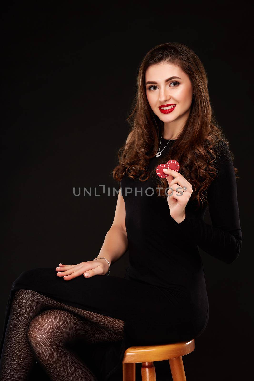 Sexy curly hair brunette posing with chips in her hands, poker concept black background by nazarovsergey