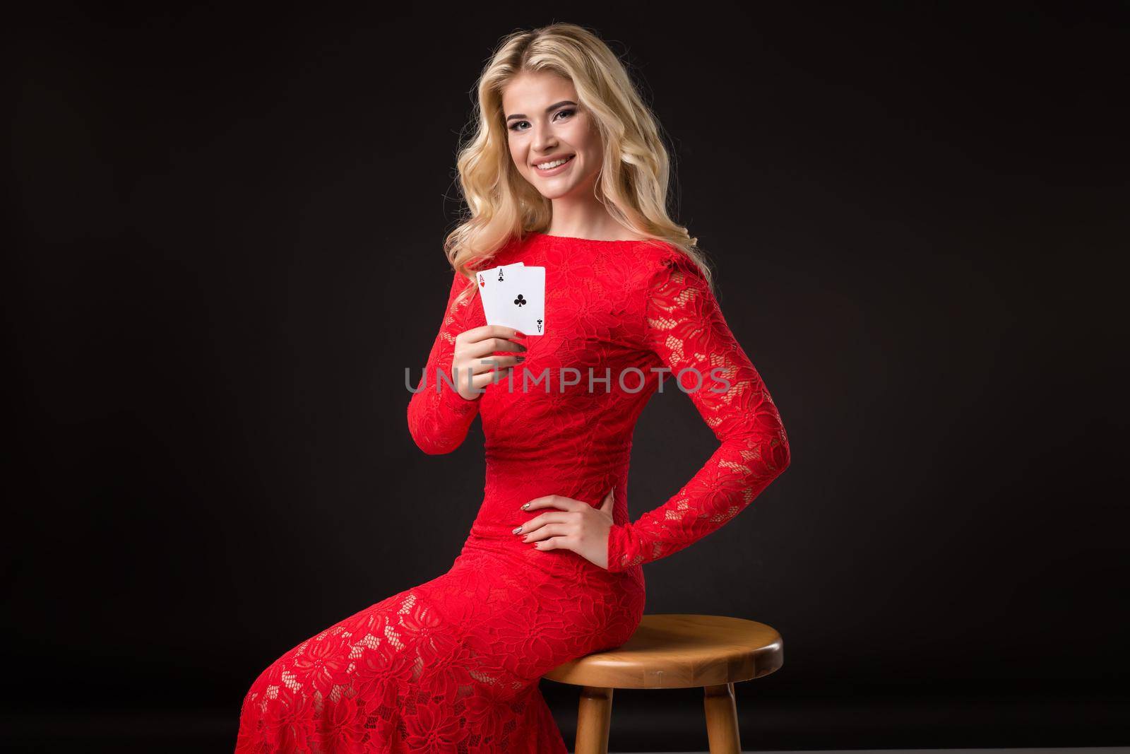 Young woman in red dress in casino with cards over black background. Poker