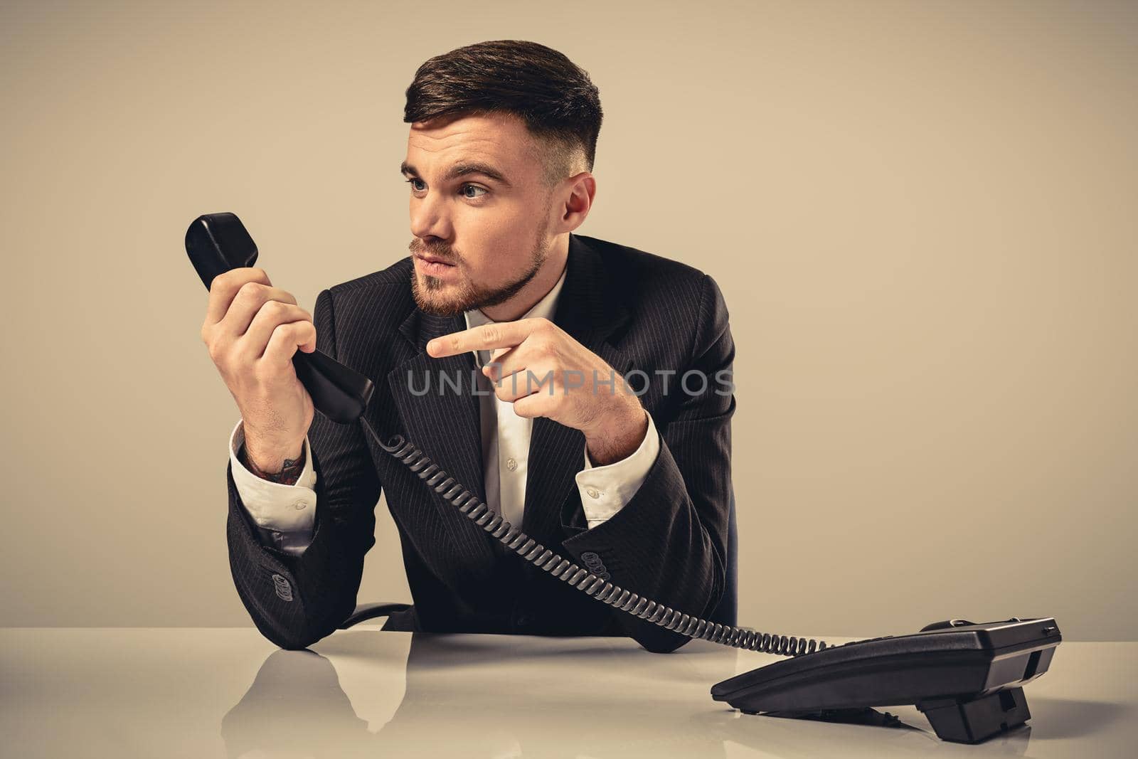 Portrait of attractive businessman holding telephone in his hand. This call is for you concept. A young man in a black suit dials the phone number while sitting in the office