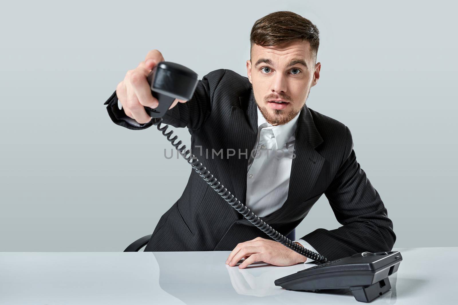 Portrait of attractive businessman holding telephone in his hand. This call is for you concept. A young man in a black suit dials the phone number while sitting in the office