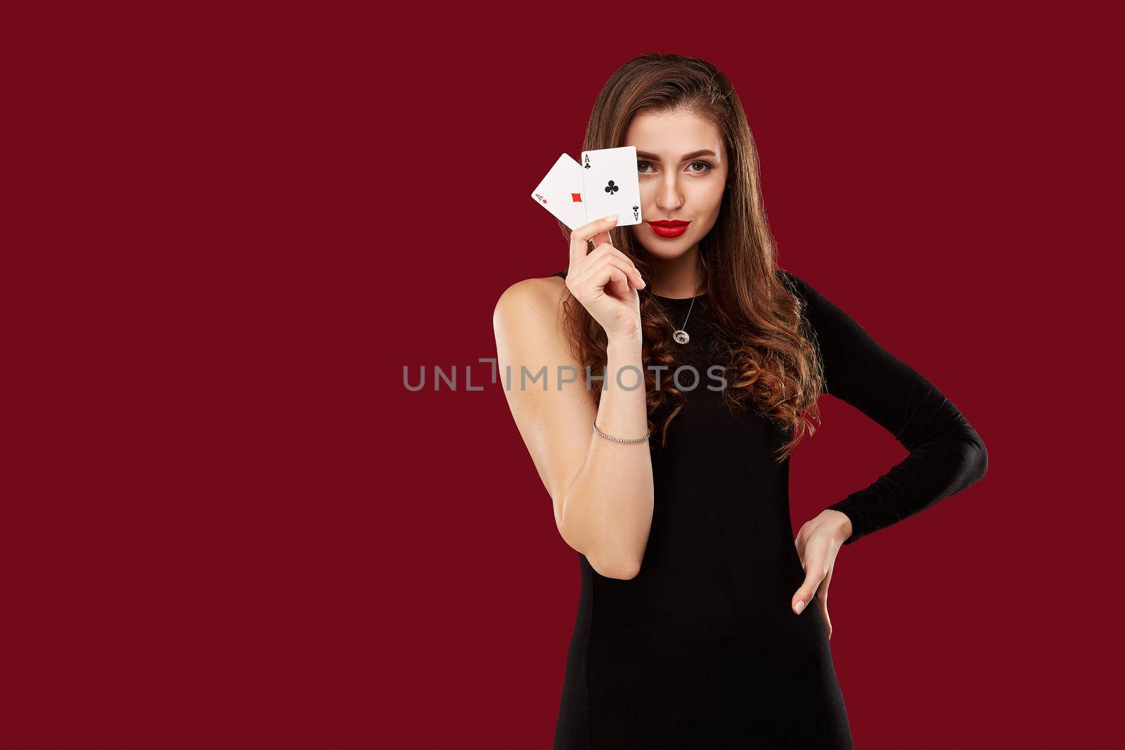 Beautiful caucasian woman in black dress with poker cards gambling in casino. Studio shot on red background. Poker. Two Aces in Hand