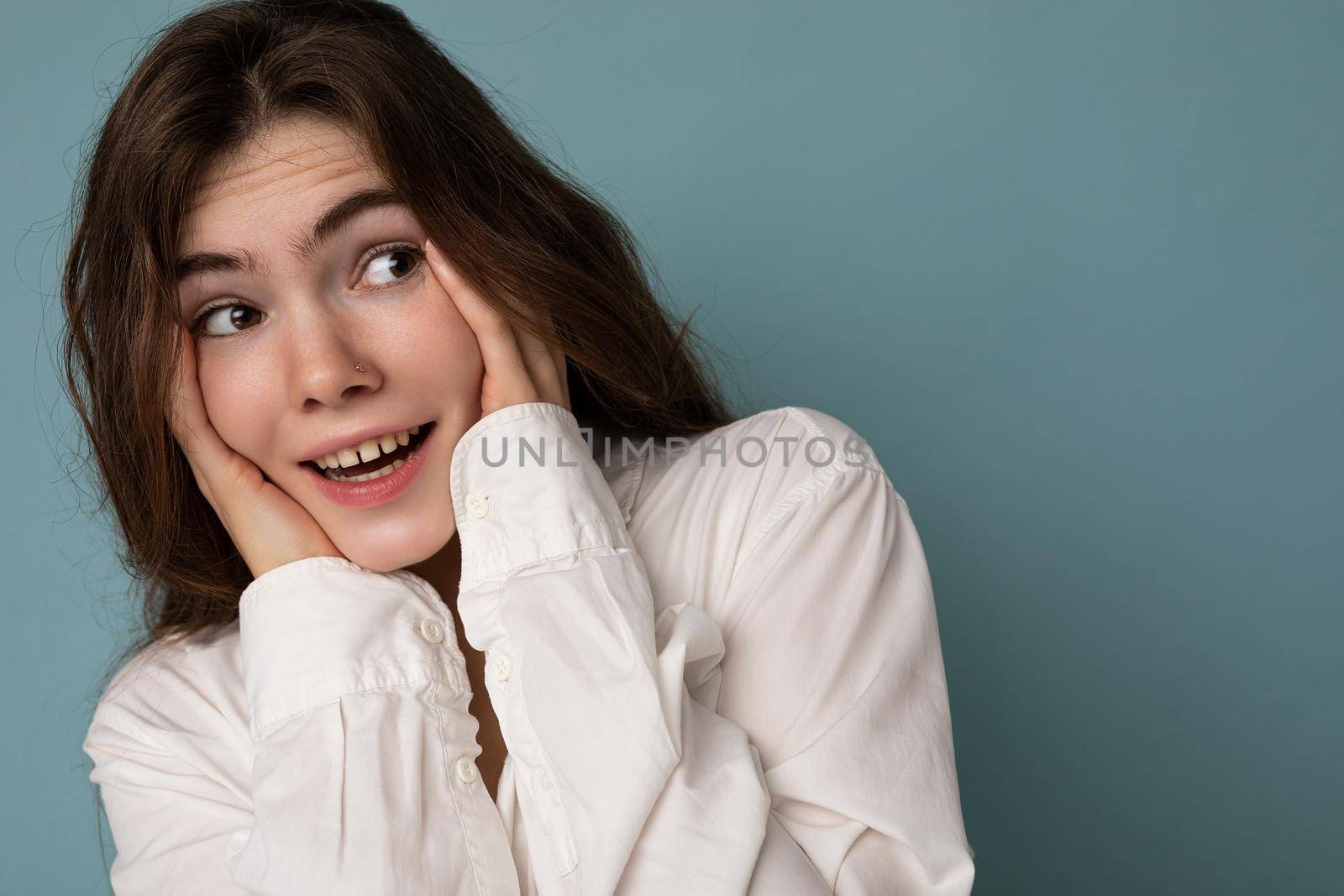 Attractive funny amusing joyful cute nice adorable tender young curly brunette woman wearing white shirt isolated on blue background with copy space by TRMK