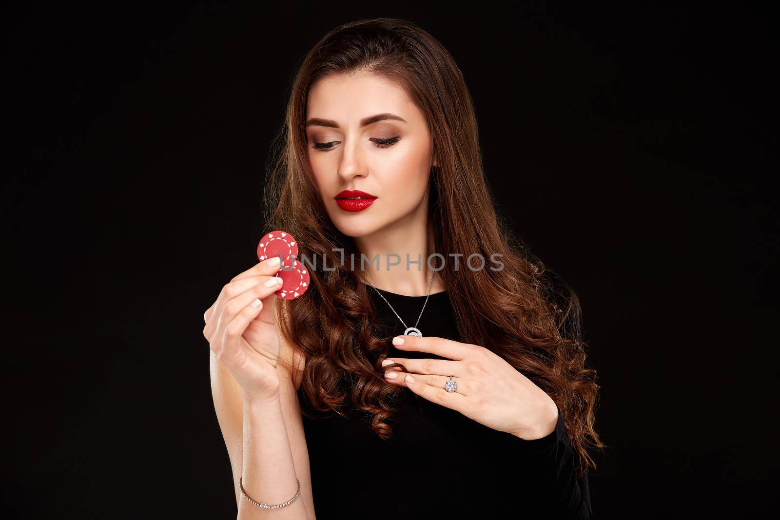 Sexy curly hair brunette in black dress posing with chips in her hands, poker concept black background. Casino, poker, Roulette Blackjack Spin.