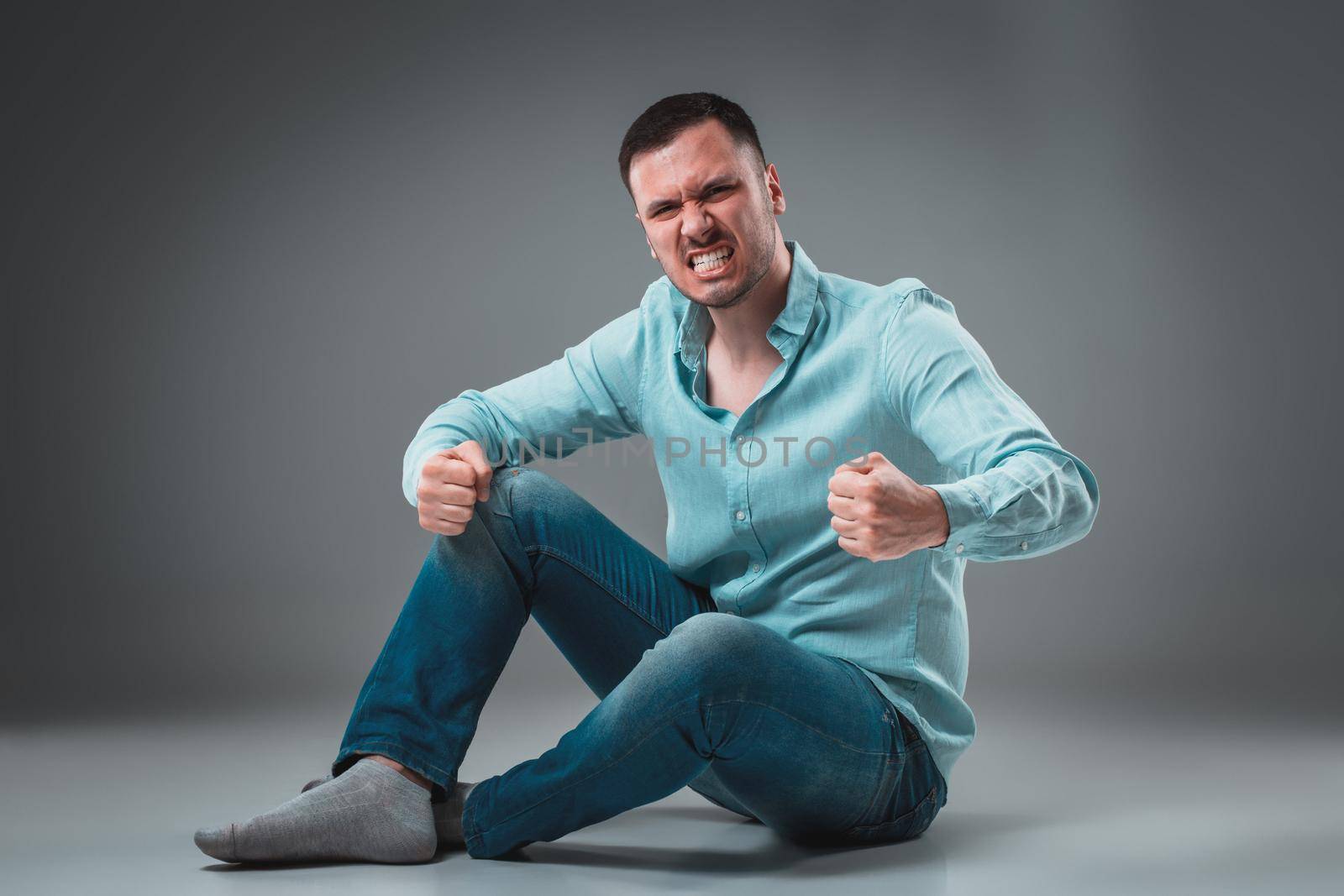 The man is sitting on the floor, isolated on gray background. Man showing different emotions. by nazarovsergey