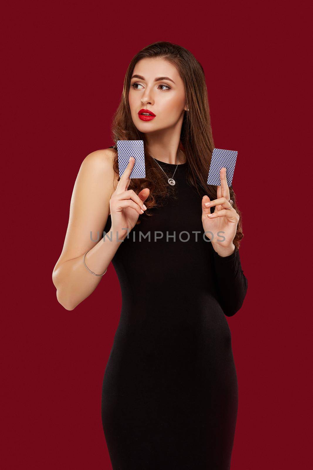 Beautiful caucasian woman in black dress with poker cards gambling in casino. Studio shot on red background. Poker. Two cards in hands