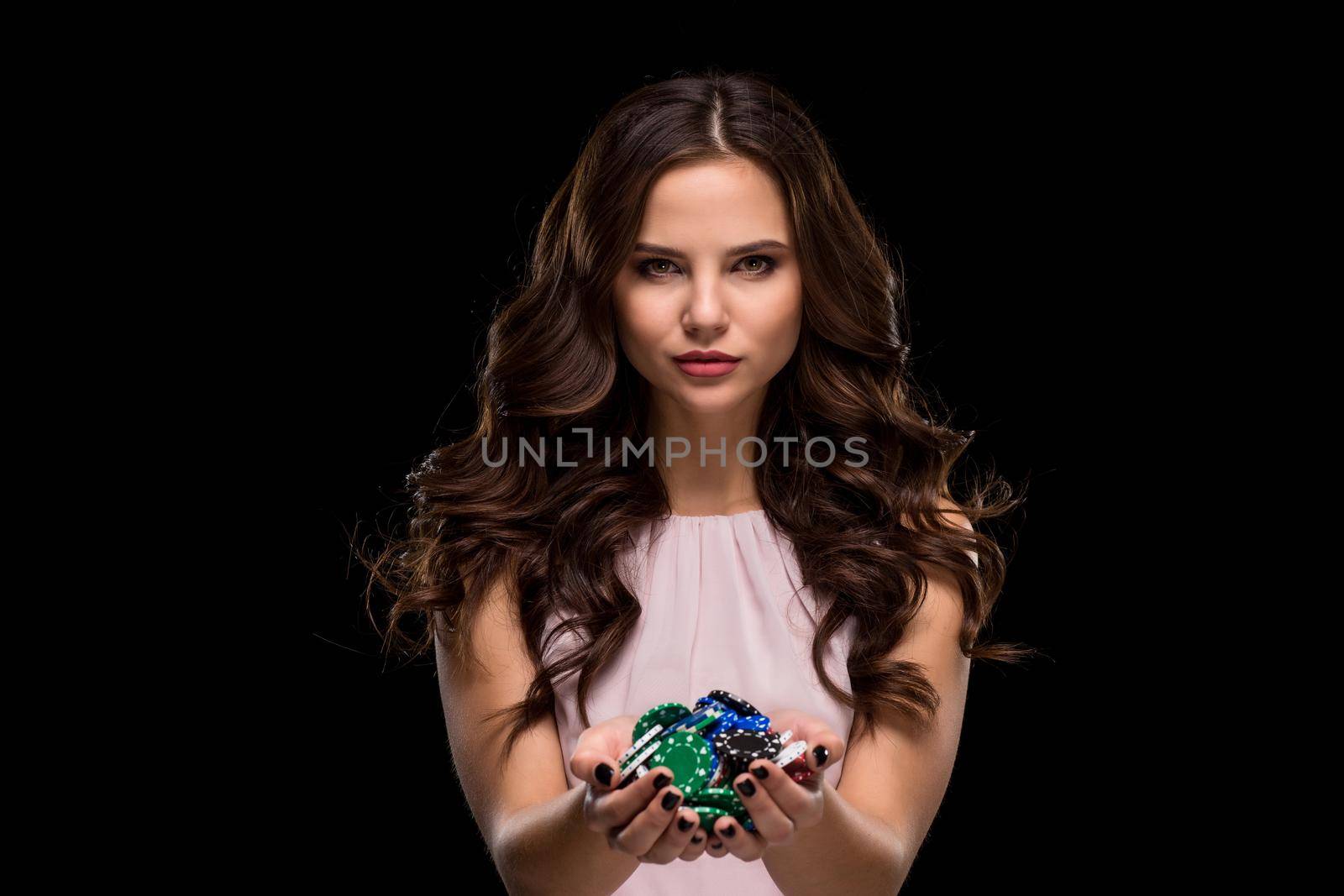 Sexy woman in a chic gently pink dress holding colored poker chips on a black background. Woman winning. Casino. Poker. Victory. Luck